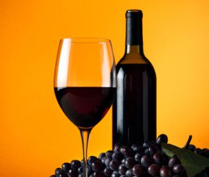 A picture of a wine glass, wine bottle and purple grapes.
