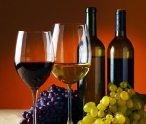 A picture of two glasses of wine, two bottles of wine, with green and purple grapes.