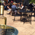 A wine bottle in the foreground with people in patio seating in the background